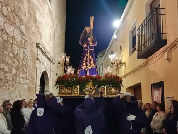 Imagen religiosa sobre andas llevada por cofrades en una calle estrecha de noche.