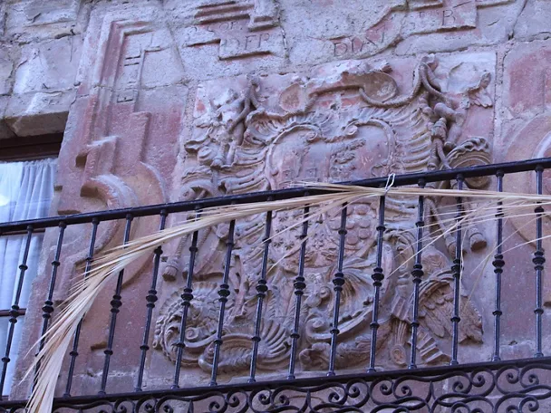 Escudo heráldico tallado en piedra sobre balcón de hierro.