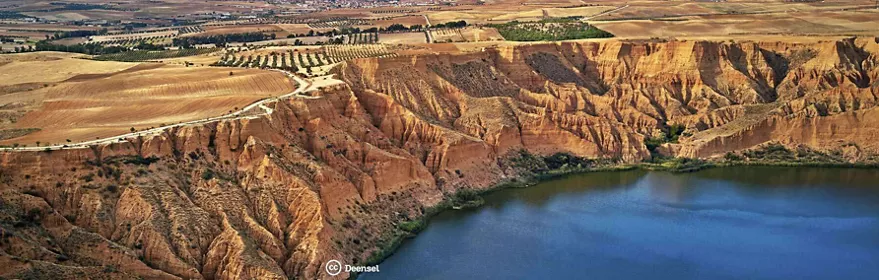 Vista aérea de cortados arcillosos junto a un embalse rodeado de campos agrícolas.