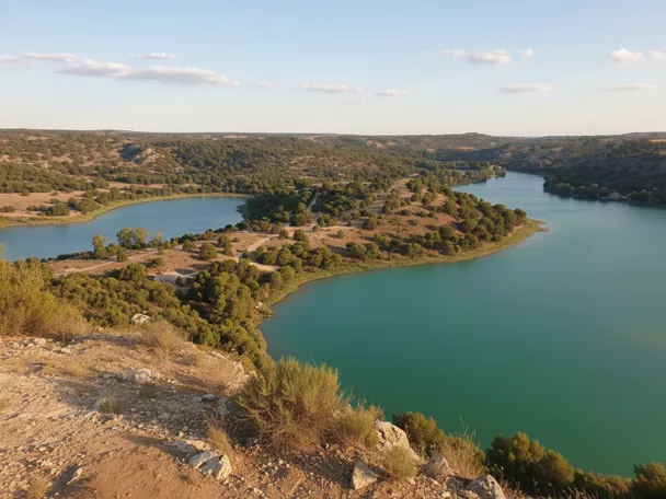 Vista panorámica de un embalse turquesa rodeado de colinas y matorral.