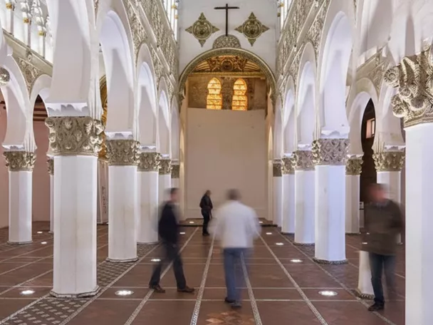 Interior de edificio histórico con columnas blancas y arcos decorados.