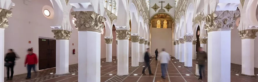 Interior de edificio histórico con columnas blancas y arcos decorados.