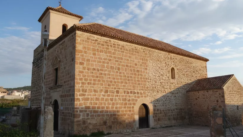 Iglesia parroquial de Socovos construida en piedra, con torre campanario y plaza adoquinada.