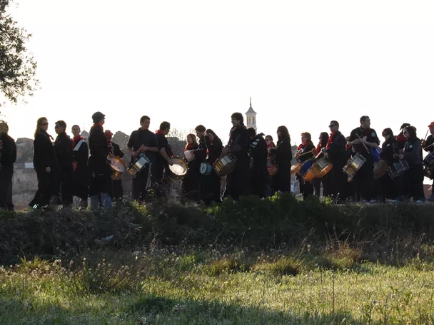 Grupo numeroso de tamborileros alineados sobre una loma con paisaje urbano al fondo.