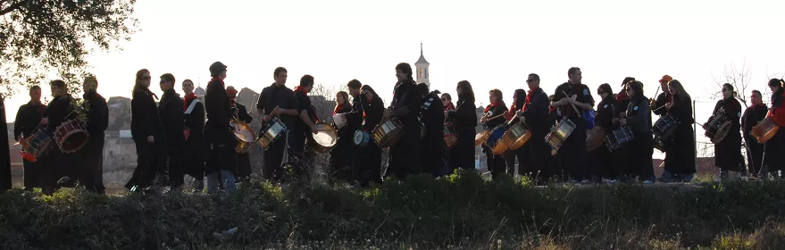 Grupo numeroso de tamborileros alineados sobre una loma con paisaje urbano al fondo.