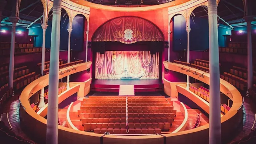 Teatro clásico con columnas y escenario iluminado visto desde el anfiteatro.