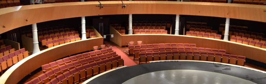 Vista panorámica de un teatro vacío con graderíos curvos y escenario central.
