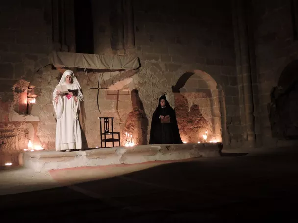 Escena teatral en iglesia con velas encendidas.