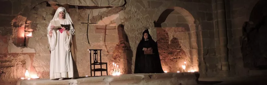 Escena teatral en iglesia con velas encendidas.