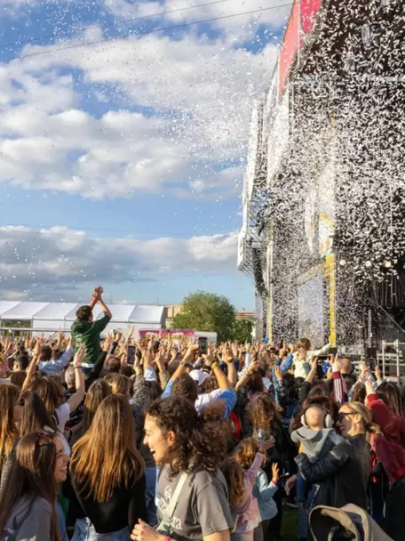 Multitud reunida frente a un gran escenario al aire libre durante un concierto.
