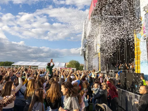 Multitud reunida frente a un gran escenario al aire libre durante un concierto.