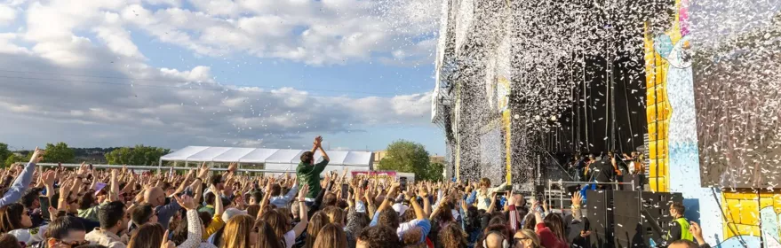 Multitud reunida frente a un gran escenario al aire libre durante un concierto.