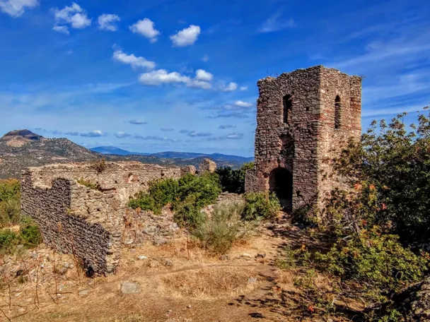 Restos de muralla y torre de piedra bajo cielo azul con nubes dispersas.