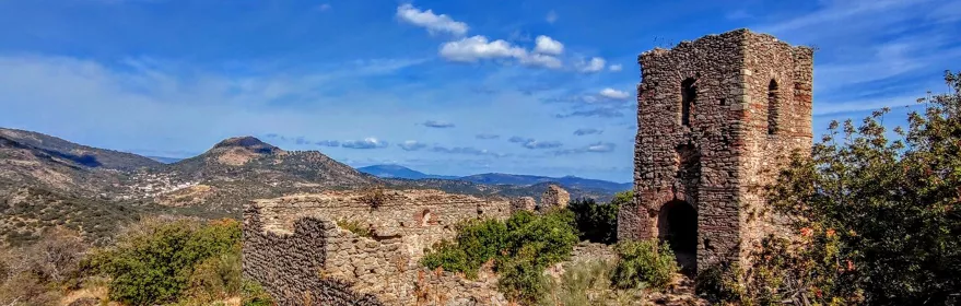 Restos de muralla y torre de piedra bajo cielo azul con nubes dispersas.