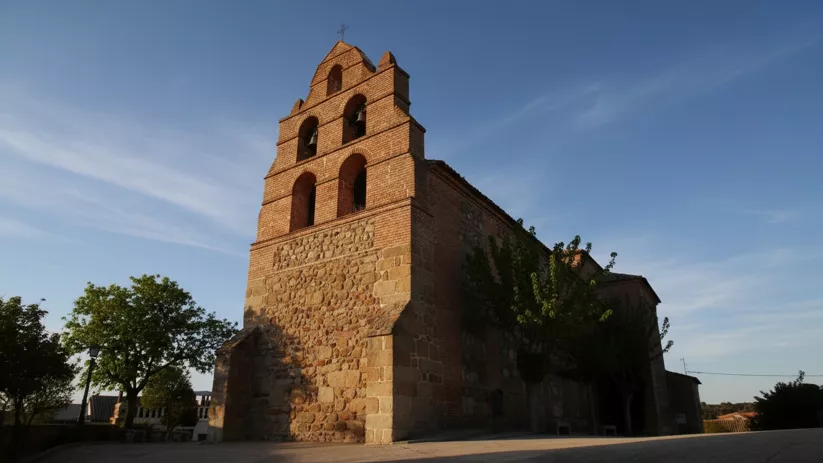 Vista en ángulo bajo de una iglesia de ladrillo y piedra con una gran espadaña de tres niveles para campanas bajo un cielo despejado.