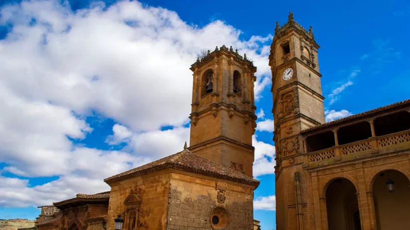 Fachada de iglesia de piedra con dos torres altas bajo un cielo azul con nubes.