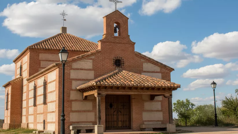 Ermita de ladrillo con espadaña y pórtico bajo cielo parcialmente nublado