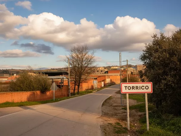 Entrada por carretera a un pequeño núcleo urbano con señal y casas bajas