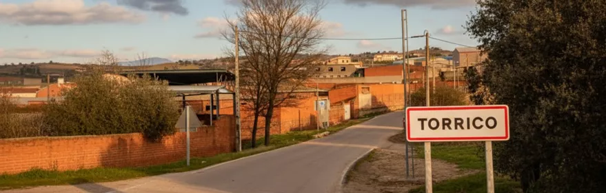 Entrada por carretera a un pequeño núcleo urbano con señal y casas bajas