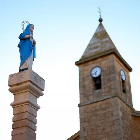 Vista de la virgen y de fondo el campanario de la iglesia