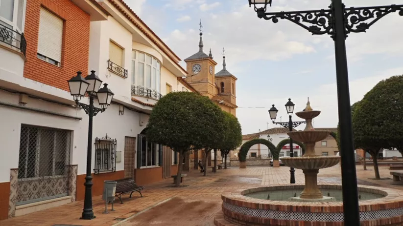 Una plaza adoquinada con una fuente de piedra de tres niveles en primer plano.