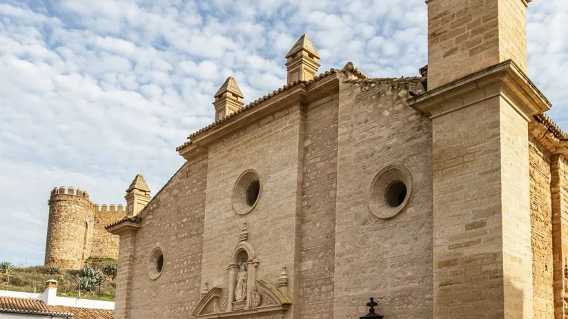 Fachada de templo de piedra con portada escultórica y torre defensiva al fondo