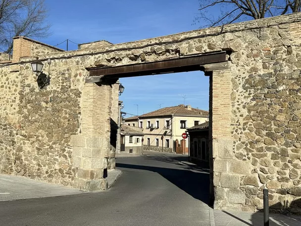 Un arco de piedra y ladrillo rústico que cruza una calle pavimentada en un entorno urbano tradicional.