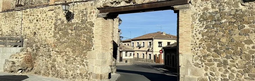 Un arco de piedra y ladrillo rústico que cruza una calle pavimentada en un entorno urbano tradicional.