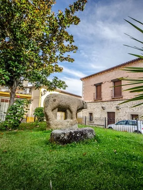 Escultura zoomorfa de piedra en una pequeña plaza rodeada de edificios.