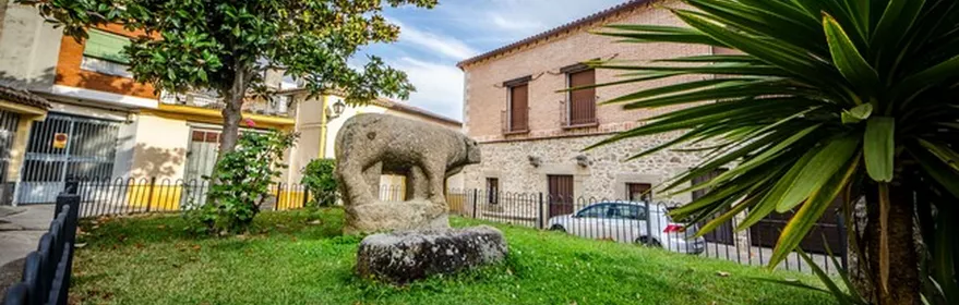 Escultura zoomorfa de piedra en una pequeña plaza rodeada de edificios.