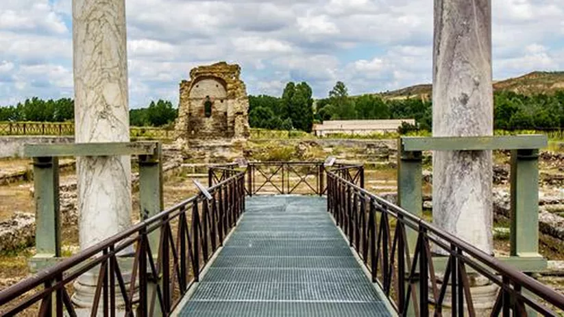 Pasarela elevada entre columnas de piedra junto a restos arqueológicos al aire libre.