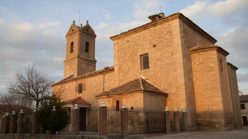 Una toma en ángulo bajo a la luz de la tarde de una iglesia de piedra rústica y su campanario adyacente, con una valla de hierro forjado y pilares de ladrillo