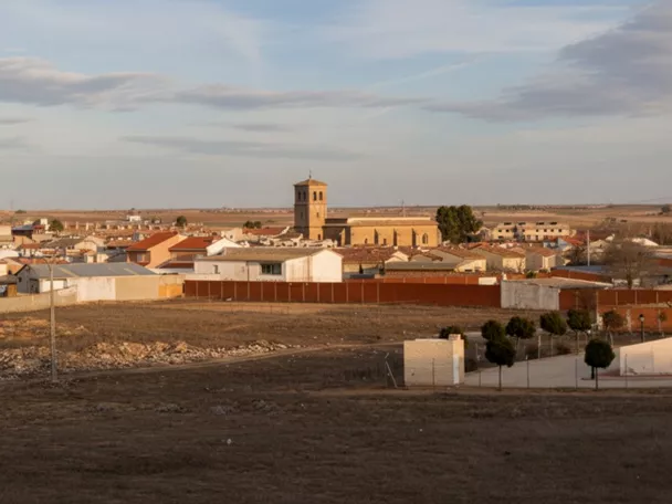 Una vista panorámica a nivel de los tejados de un pueblo con una torre de iglesia de ladrillo a la derecha, vista desde un campo árido.