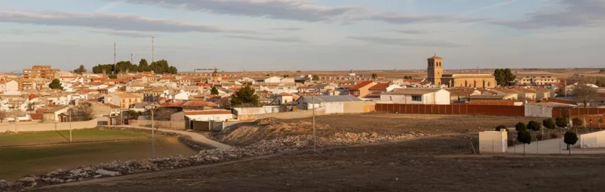 Una vista panorámica a nivel de los tejados de un pueblo con una torre de iglesia de ladrillo a la derecha, vista desde un campo árido.