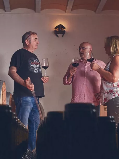 Personas tomando una copa de vino rodeados de botas y botellas de vino