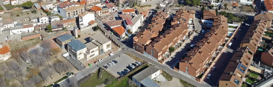 Una amplia vista panorámica de una plaza de pueblo vacía flanqueada por edificios históricos blancos y de ladrillo bajo un cielo parcialmente nublado.