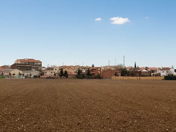 Panorámica de campo arado frente a un núcleo urbano bajo cielo despejado.