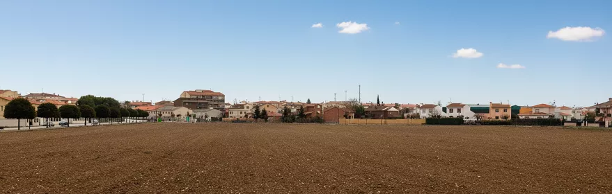 Panorámica de campo arado frente a un núcleo urbano bajo cielo despejado.