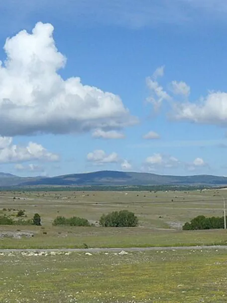 Panorámica de campos abiertos con colinas suaves y cielo con nubes dispersas.