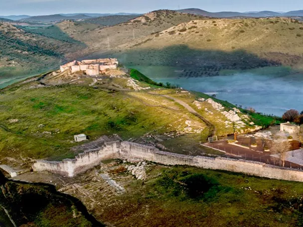 Vista aérea de fortaleza en colina rodeada de campos verdes y niebla baja
