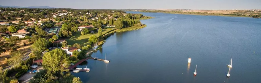 Vista aérea de un embalse con orilla arbolada, embarcaciones y zonas verdes