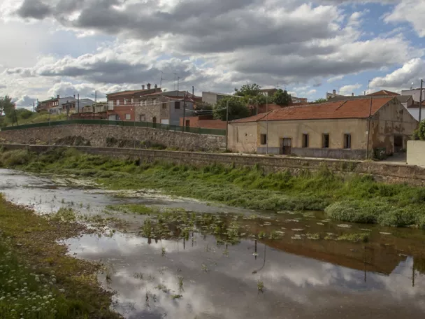 Vista del casco urbano junto a un río con casas tradicionales y cielo nublado.