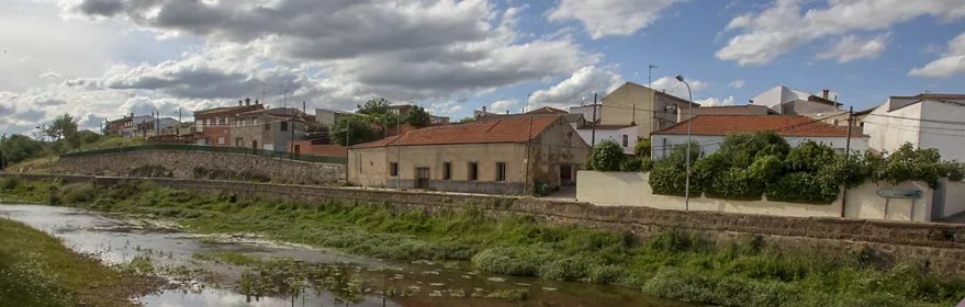 Vista del casco urbano junto a un río con casas tradicionales y cielo nublado.