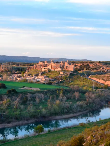 Vista panorámica de valle con río, campos verdes y conjunto histórico en lo alto
