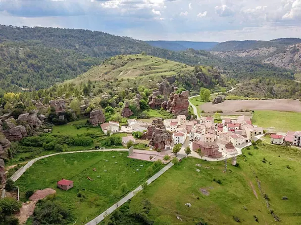 Pequeño pueblo entre prados verdes y formaciones rocosas.