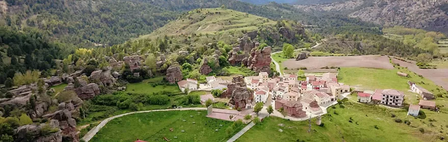 Pequeño pueblo entre prados verdes y formaciones rocosas.