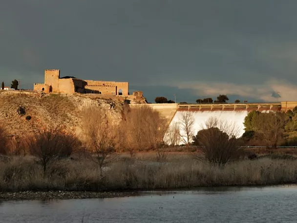 Fortaleza de piedra junto a presa y lámina de agua al atardecer