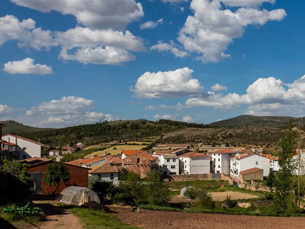 Vista panorámica de un pequeño pueblo rodeado de campos verdes y colinas bajo un cielo con nubes.