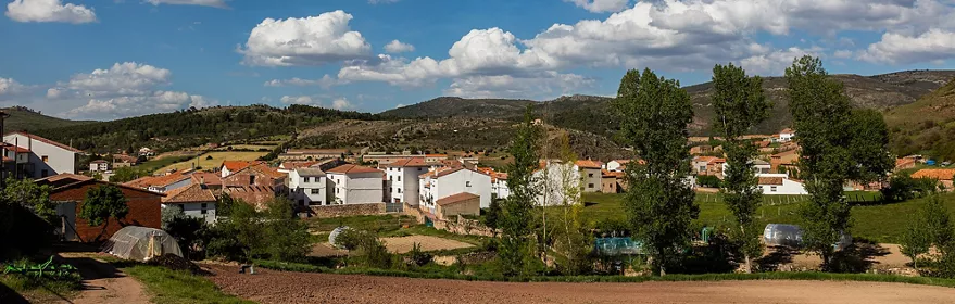 Vista panorámica de un pequeño pueblo rodeado de campos verdes y colinas bajo un cielo con nubes.