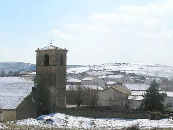 Panorámica de un pueblo cubierto de nieve con torre de iglesia y casas.